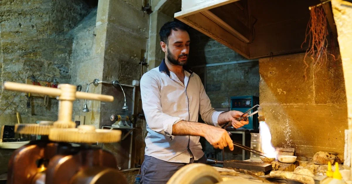 Artisan qualifié travaillant avec des outils et une flamme dans un atelier de bijouterie traditionnel.