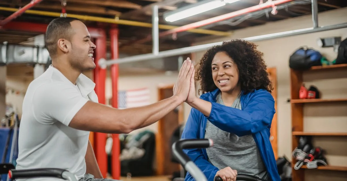 Deux personnes diverses se donnant une tape dans la main lors d'une séance d'entraînement énergique dans une salle de sport, mettant en avant la motivation et le travail d'équipe.