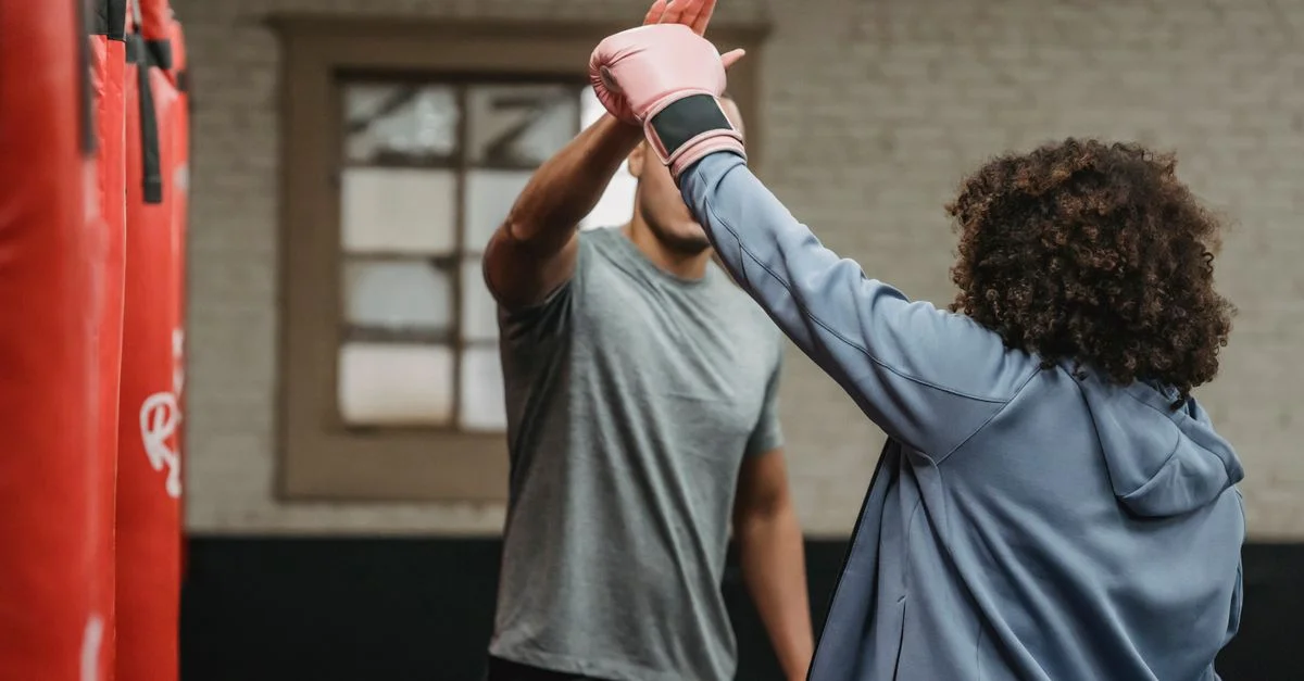 L'entraîneur de boxe et l'apprentie se donnent un high five pendant l'entraînement dans une salle de sport intérieure.