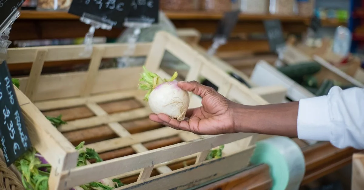 Gros plan sur une main sélectionnant un navet frais dans une caisse en bois au marché portugais.